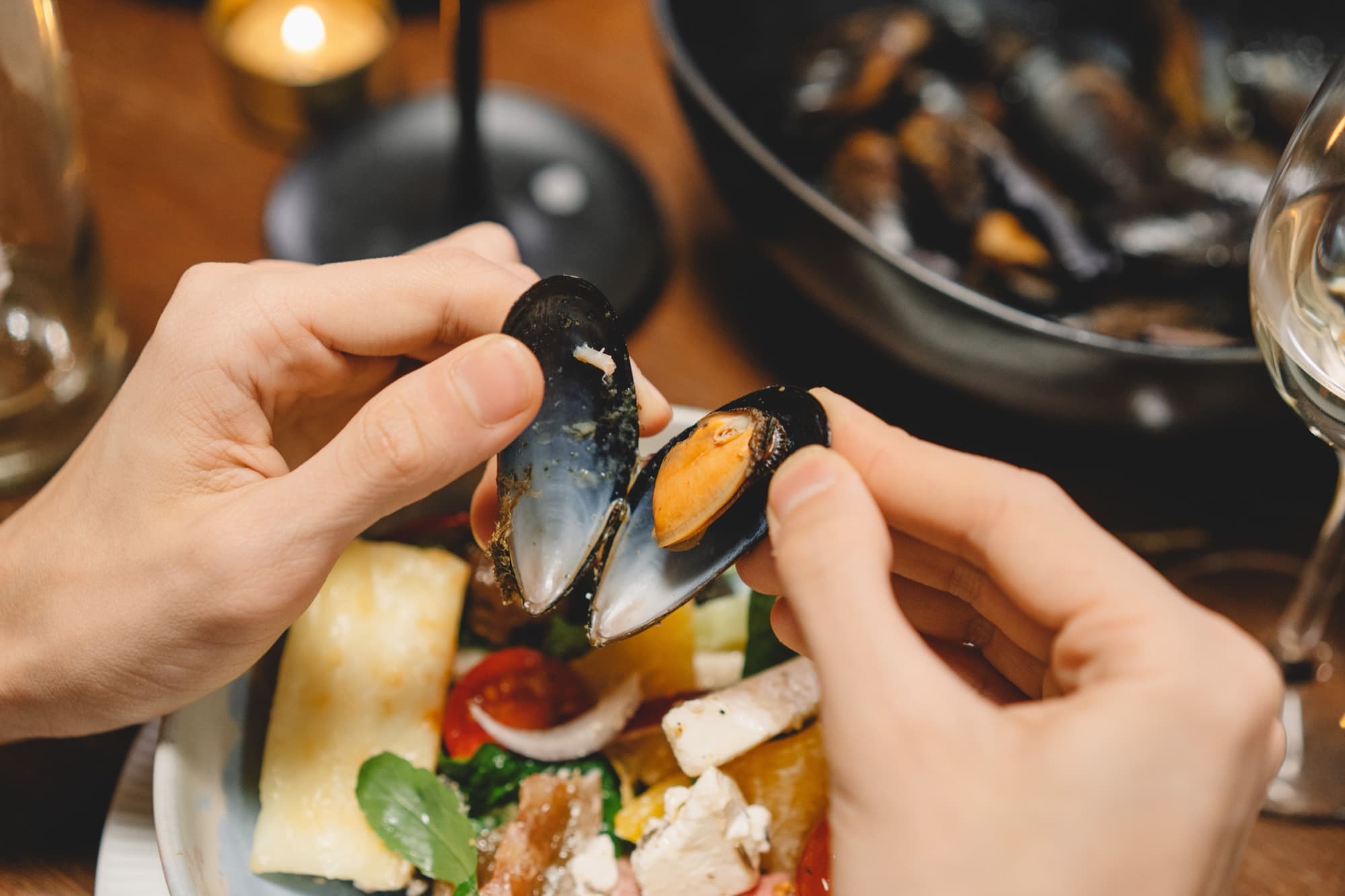 A diner opening a mussel at a candlelit table